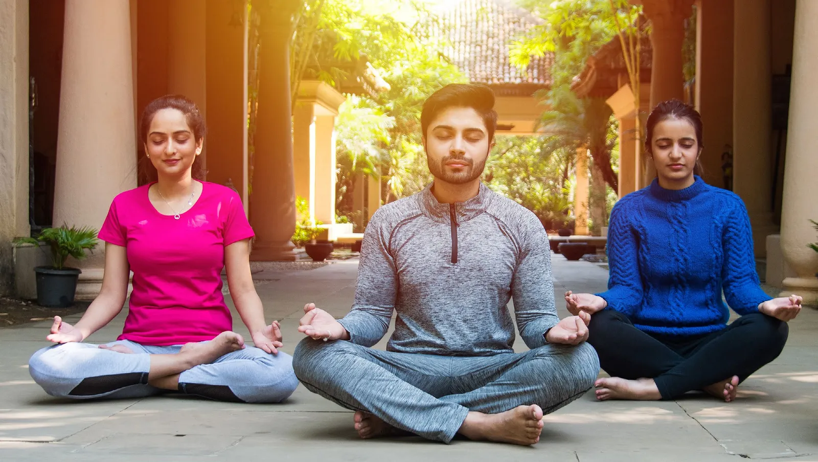 Three educators meditating cross-legged in a sunlit colonnade