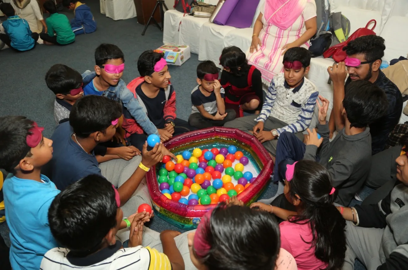 Blindfolded children sitting around a ball pit, sorting coloured balls