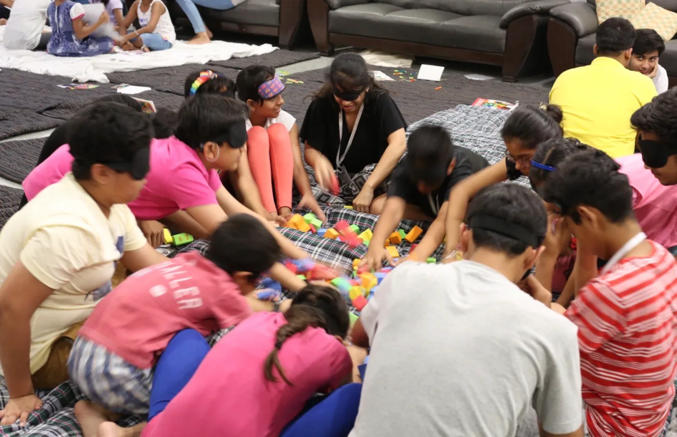 Blindfolded children around a pile of coloured foam blocks
