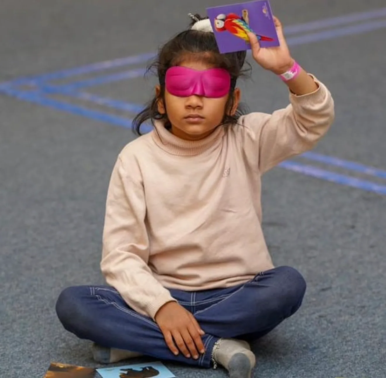 A blindfolded girl sitting cross-legged, holding up a picture card of a parrot