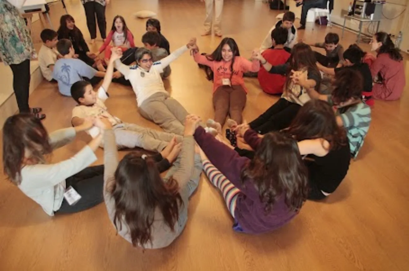 Children and Shreya sitting in a circle on the floor, holding hands