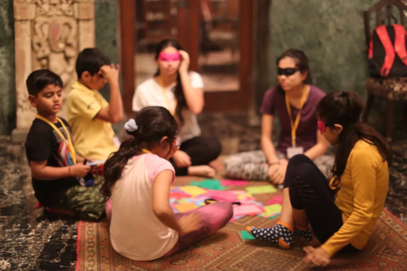 Children in eye masks sitting around colourful paper cards on a rug
