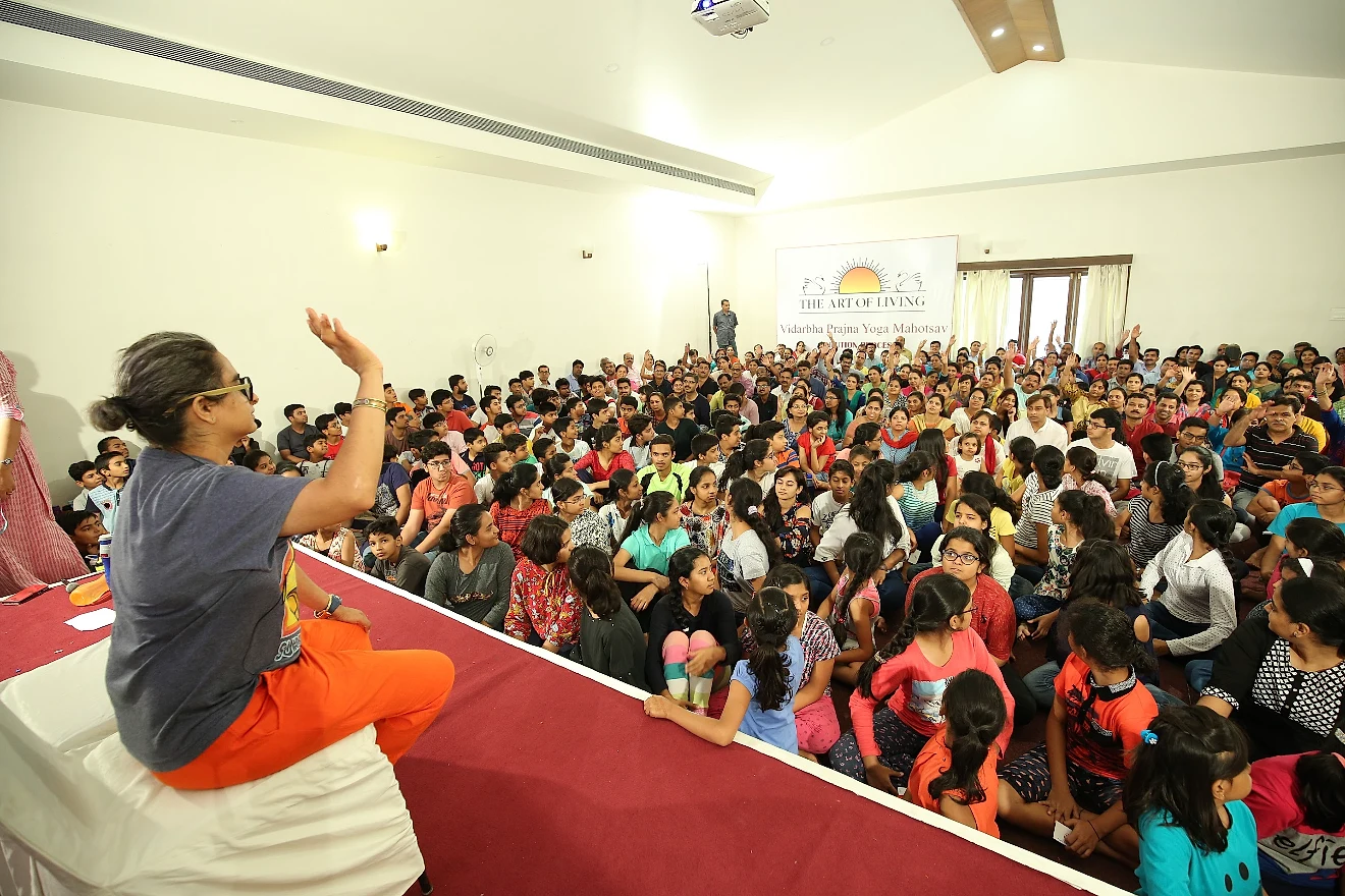 Shreya on stage before a packed hall of children and parents at a Prajna Yoga Mahotsav