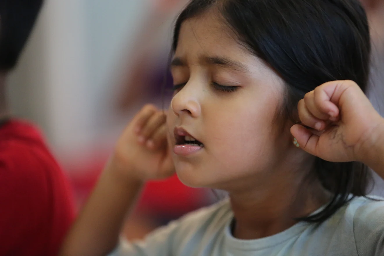 A young girl with her eyes closed and fingers in her ears, doing the humming-bee breath