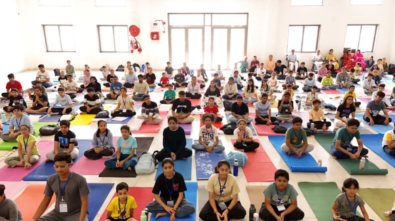 A large hall full of children and teens meditating on colourful yoga mats