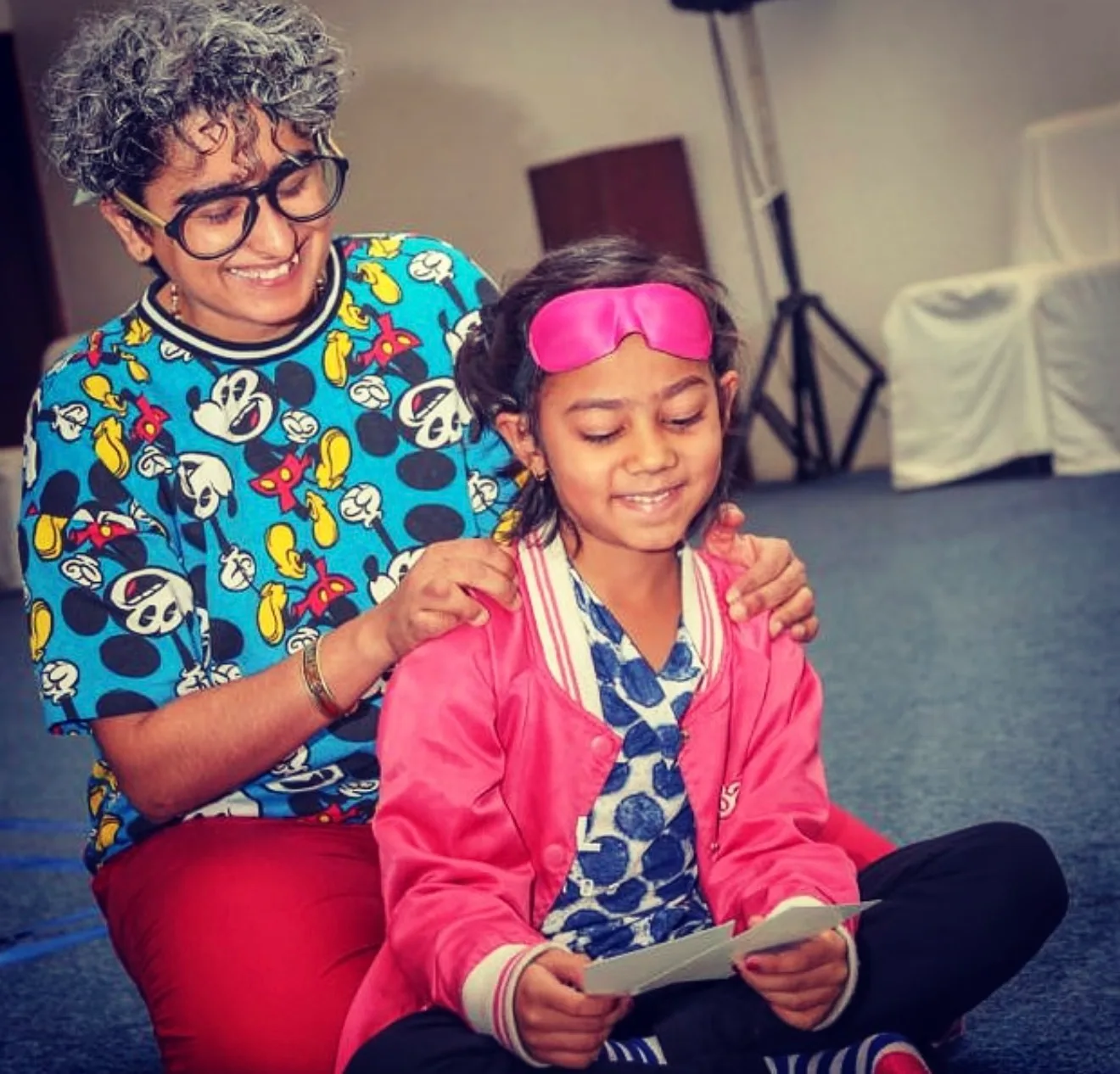 Shreya with her hands on a smiling girl's shoulders as she looks at picture cards