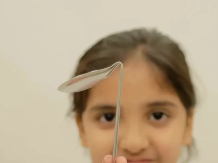 A young girl holding up a spoon whose bowl is bent right back