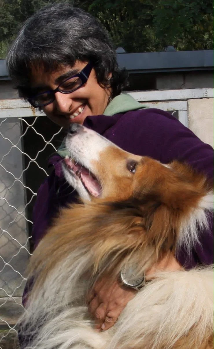 Shreya laughing as a big fluffy sable and white dog leans back into her arms