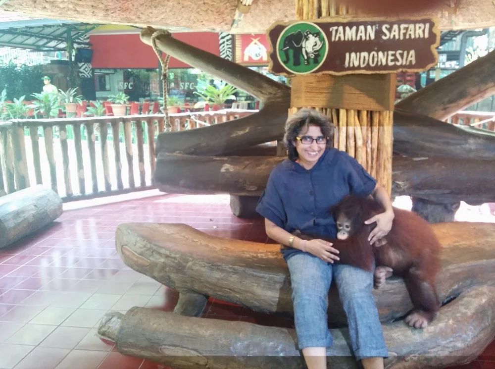 Shreya smiling on a log bench at Taman Safari Indonesia with a young orangutan on her lap