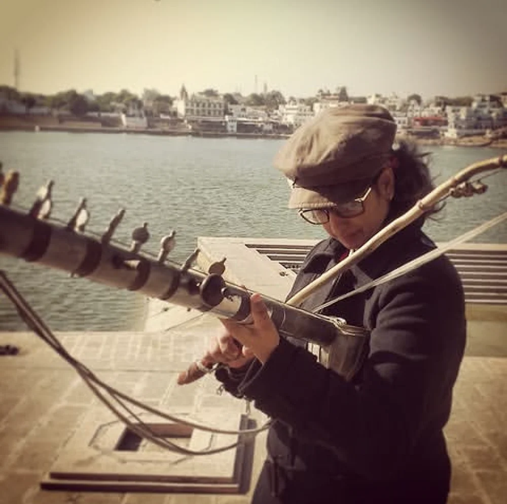 Shreya in a cap playing a long-necked string instrument on the ghats of Pushkar lake