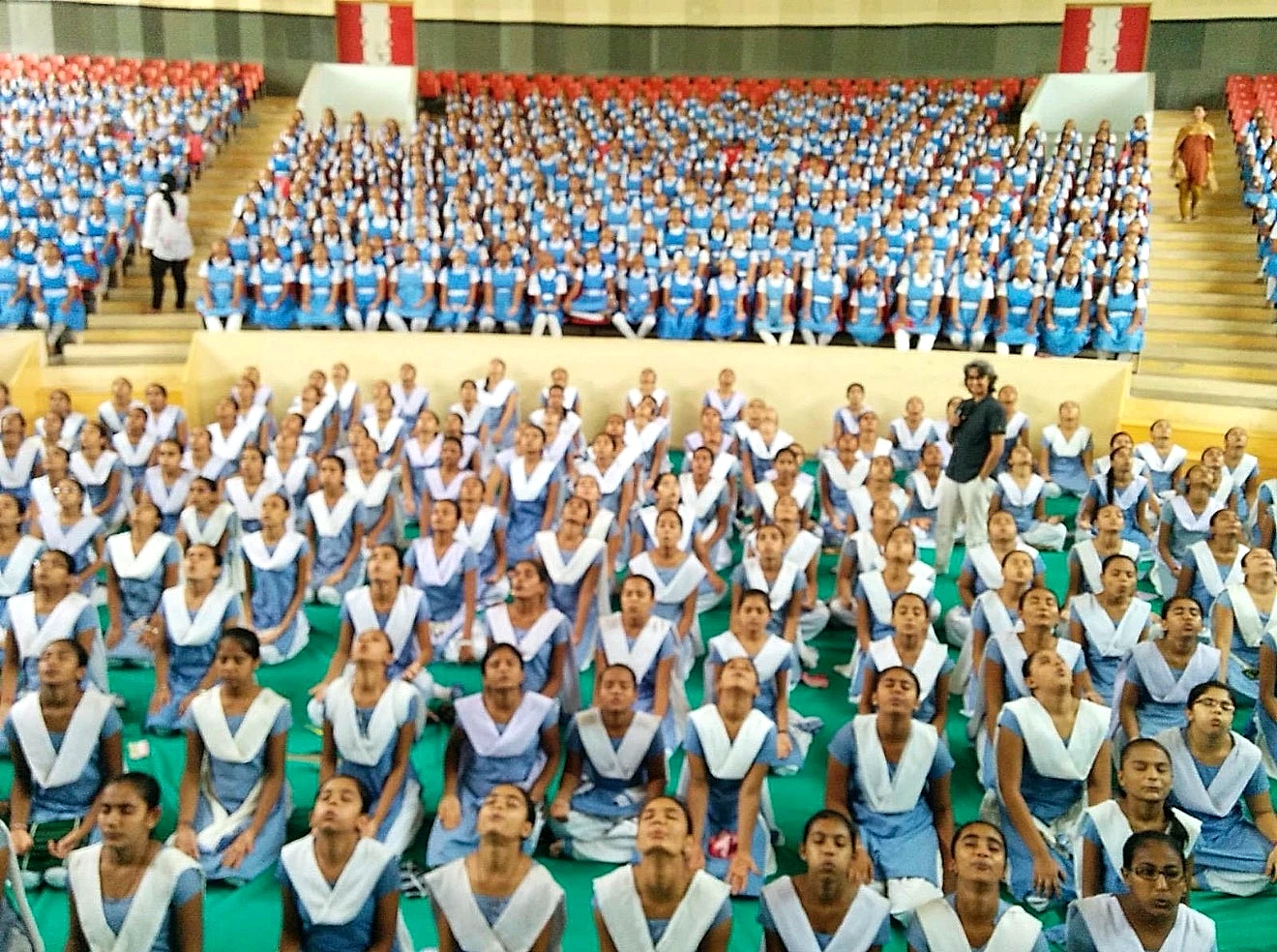 Shreya guiding hundreds of schoolgirls in blue uniforms through a breathing practice in a packed hall