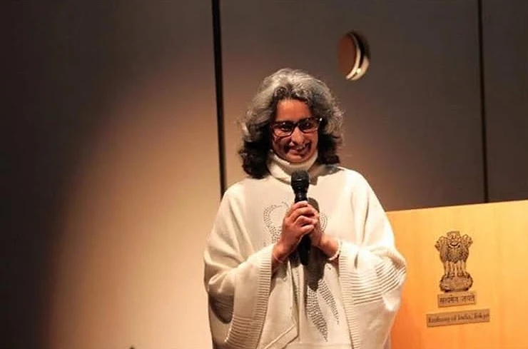 Shreya smiling as she speaks into a microphone at the Embassy of India in Tokyo, beside a lectern bearing the Indian national emblem